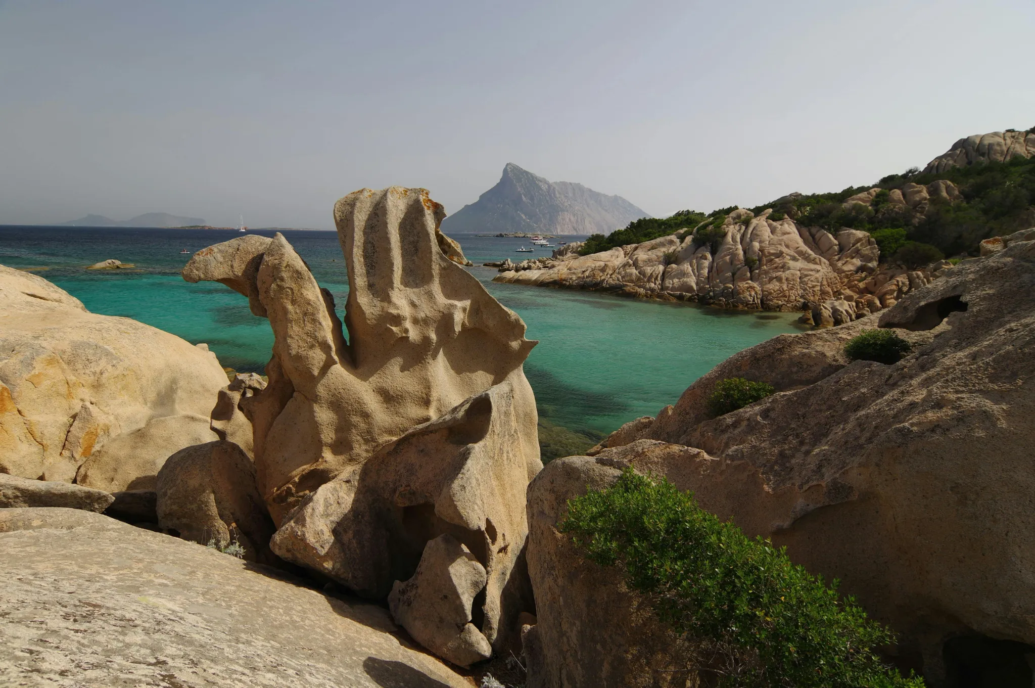 Costa rocciosa della Sardegna con mare turchese e profilo montuoso sullo sfondo